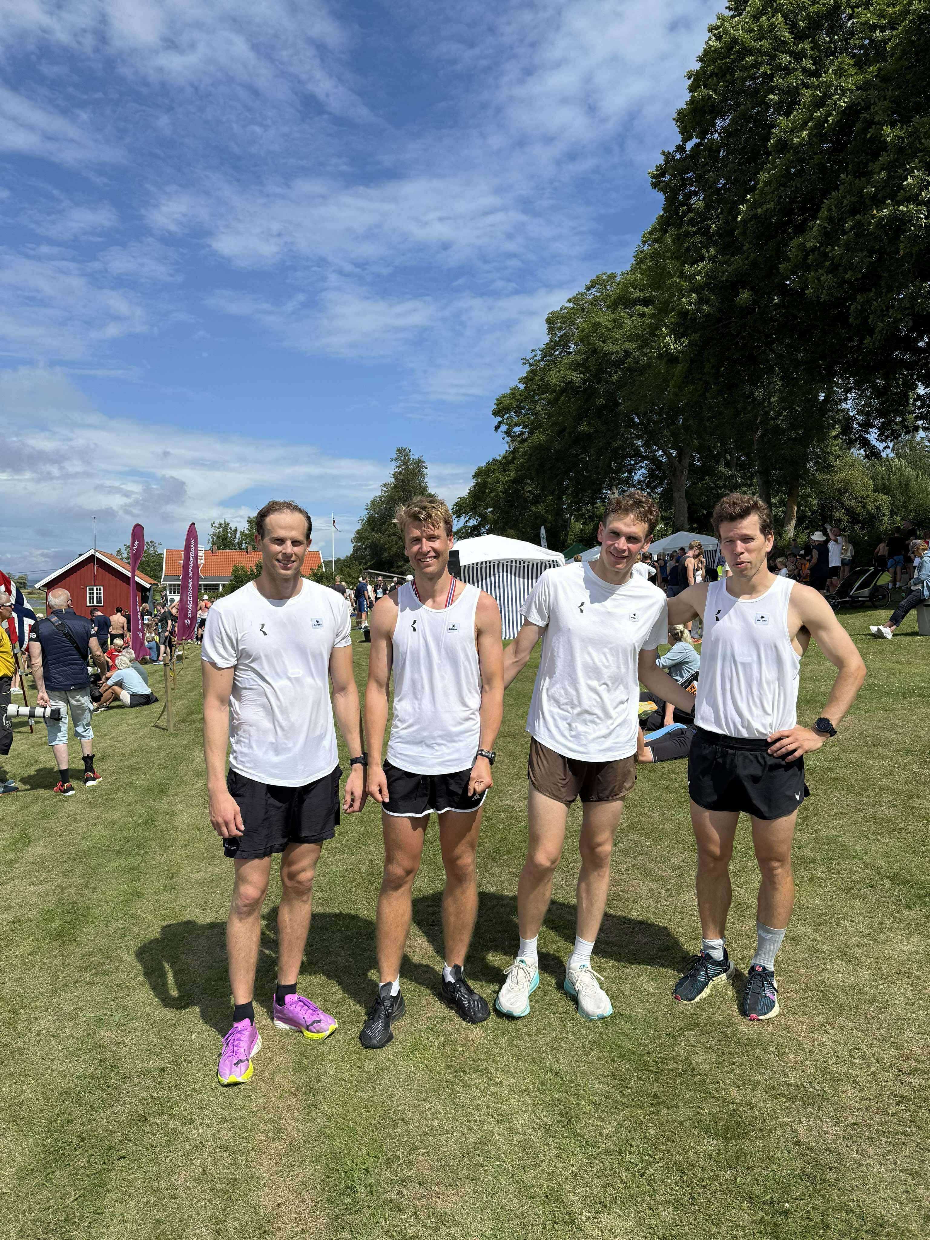 Fire venner i hvite t-skjorter med Kil Tennis & Kulturklubb-logo, ute på en sommerdag.